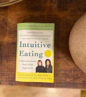 Intuitive Eating Book 4th Edition sitting on dark wood cabinet top