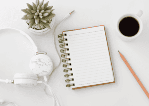 white counter top, blank white spiral notebook open in middle, number 2 pencil and cup of coffee on the right. small succulent plan and white headphones to the left. Space to explore binge eating disorder support.