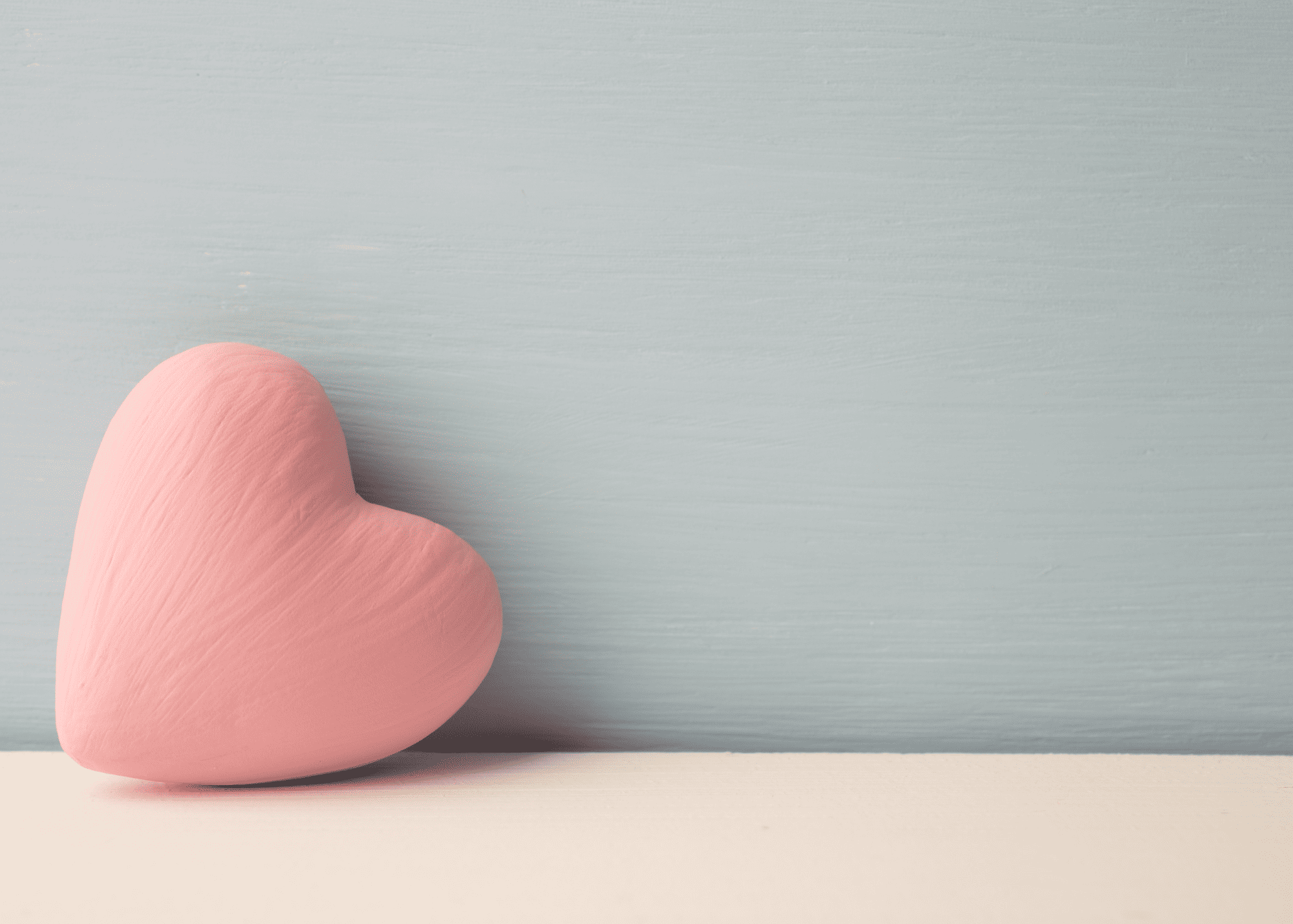 light wood surface with baby blue background. Large pink heart resting on it's side.