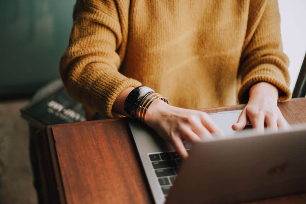 women in yellow sweater typing on laptop