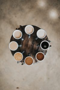 coffee mugs in a circle on a circular table ranging from black coffee and increasing in amount of milk added around the circle. 