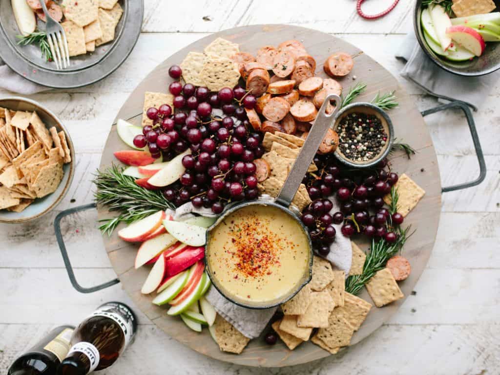 Round platter of holiday snacks including purple grapes, crackers, apple slices dip, cherries and salami pieces. Food over the holidays. 